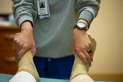 Mains d'un kinésithérapeute travaillant la jambe d'un patient en séance
